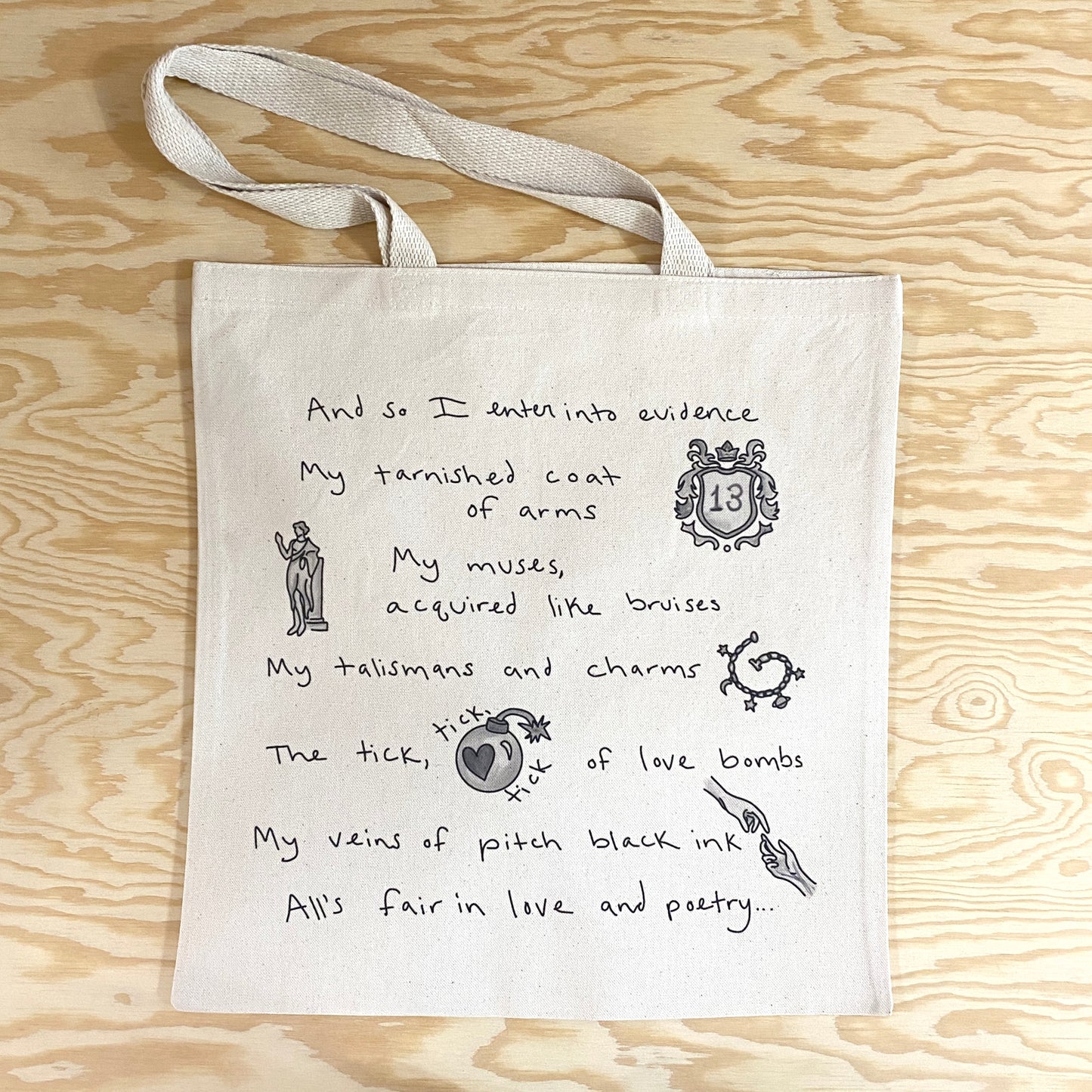 A canvas tote bag with song lyrics from The Tortured Poets Department album by Taylor Swift. The text reads: And so I enter into evidence my tarnished coat of arms, my muses, acquired like bruises, my talismans and charms, the tick, tick, tick of love bombs, my veins of pitch black ink, all's fair in love and poetry...