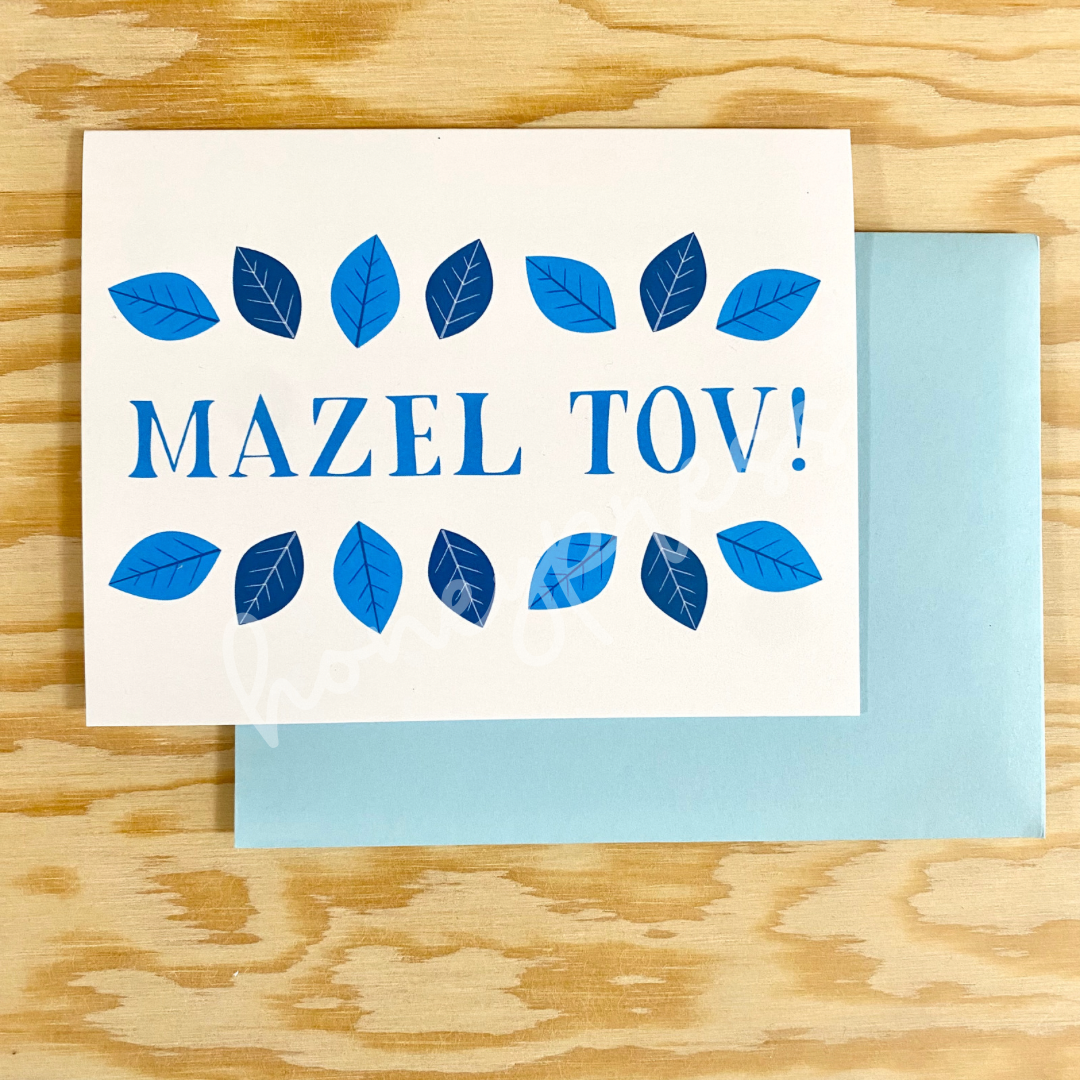 A white card with a blue envelope. The card reads "Mazel Tov!" in blue letters, with blue leaves along the top and bottom of the words.