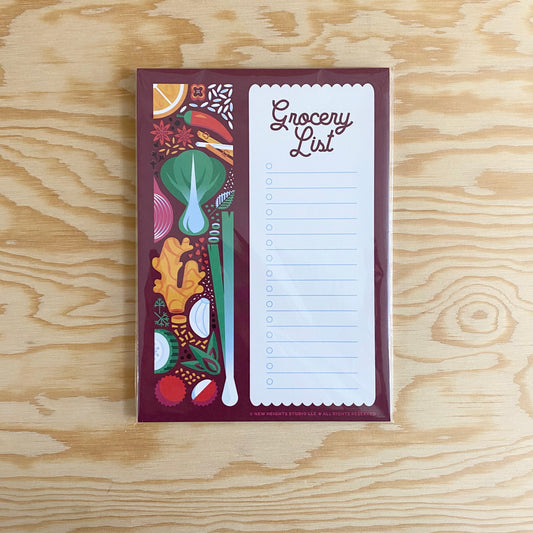 A maroon notepad with different Asian food ingredients on the left side. On the right side is a white scalloped box with the words "Grocery List" in cursive on the top of the box.