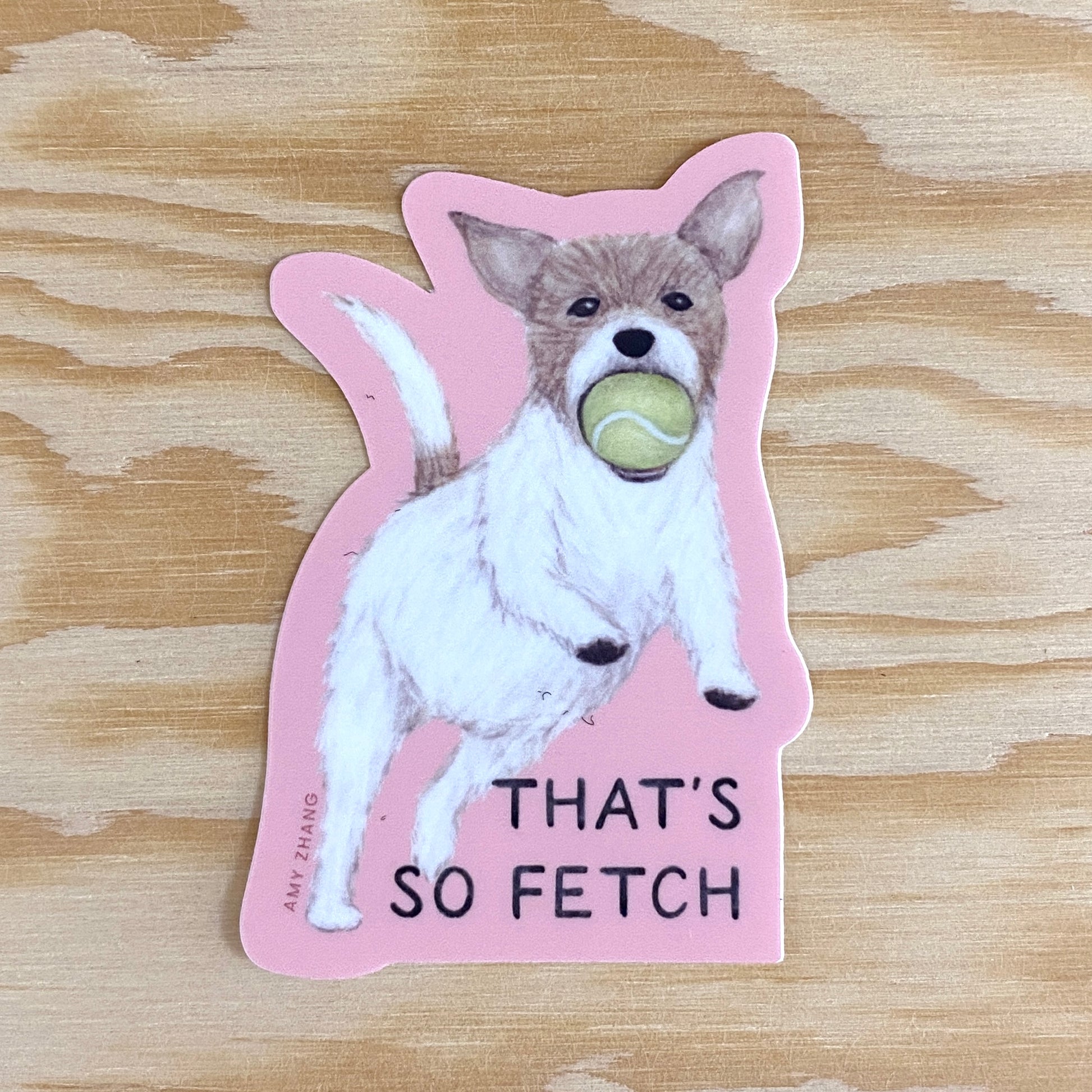 A vinyl sticker with a furry puppy catching a tennis ball in its mouth and a pink background. The text reads: That's so fetch (which is a quote from the movie, Mean Girls).